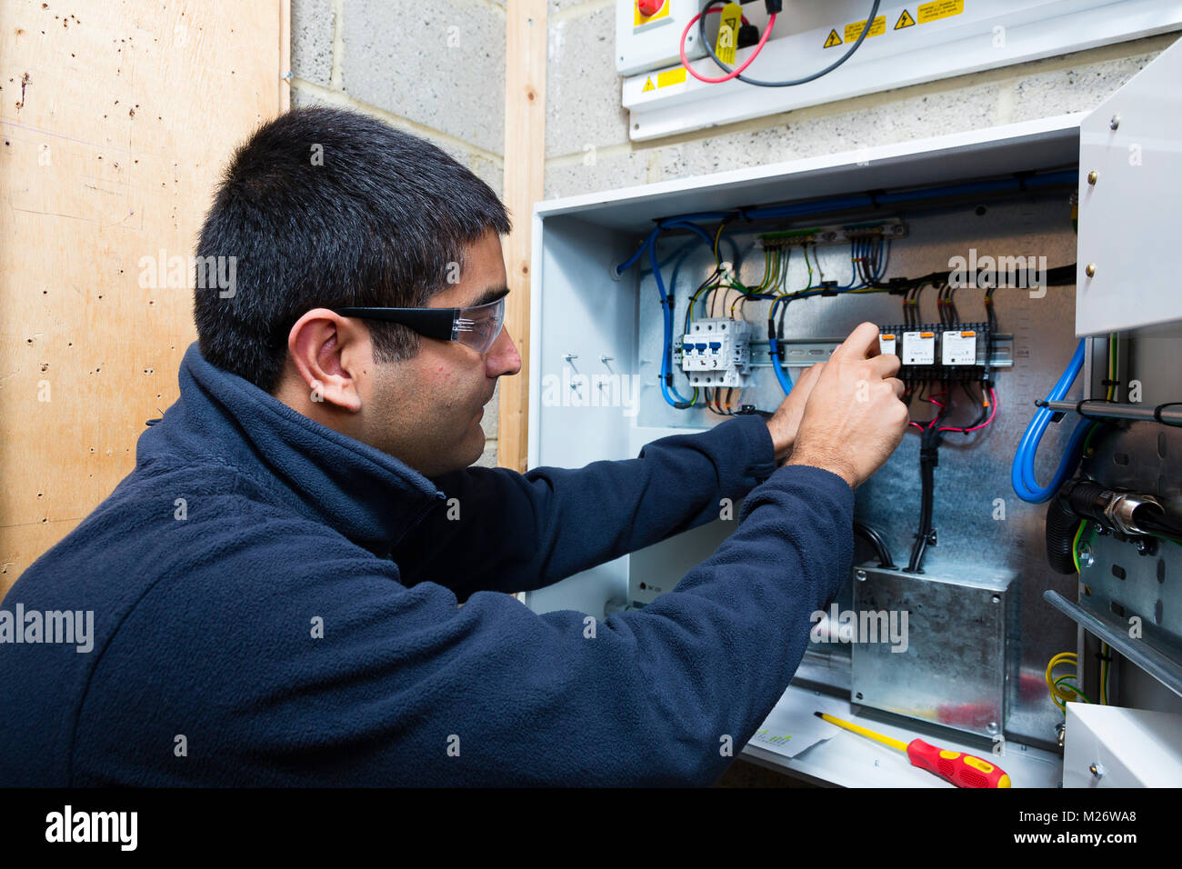 A young Asian apprentice electrician works with a screwdriver at a junction box. Stock Photo
