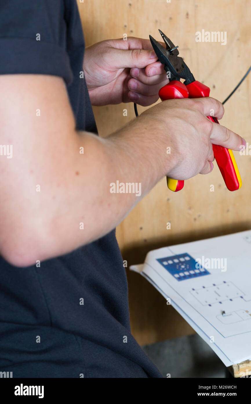 A young man uses a pair of pliars to cut an electrical cable. Stock Photo