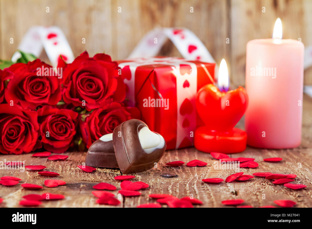 Chocolate pralines in front of bouquet of red roses and candles on wooden background. Valentines day concept. Motherâ€™s day concept! Focus on praline Stock Photo