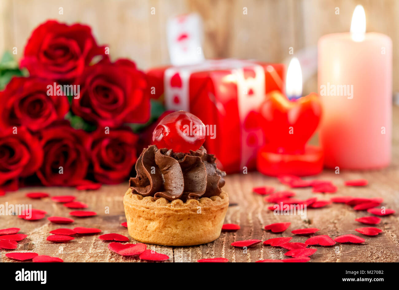 Cupcake with cherry in front of bouquet of red roses and candles on wooden background. Valentines day concept. Focus on cake! Stock Photo