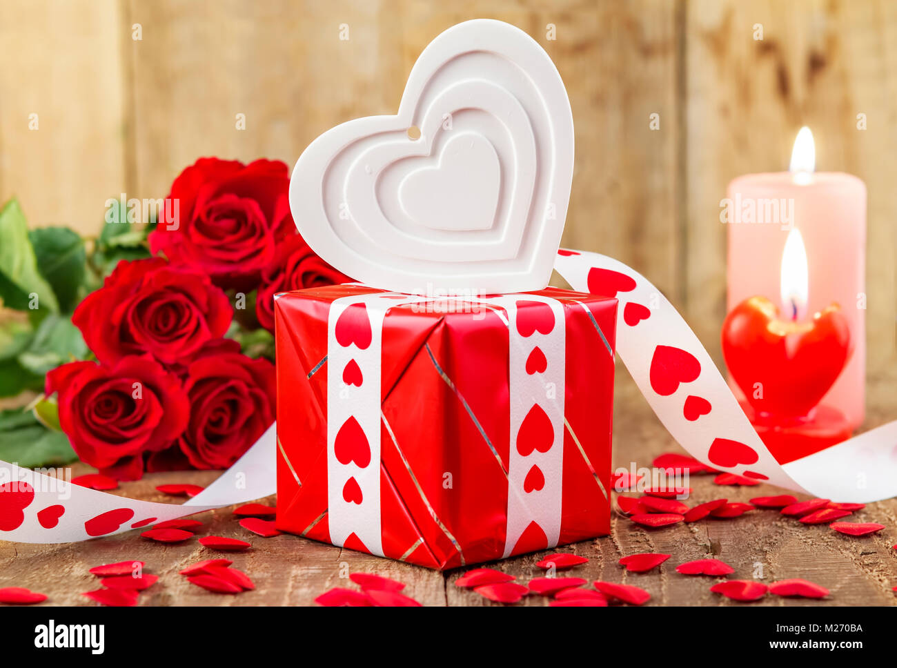 Shape of white heart over gift box in front of bouquet of red roses and candles on wooden background. Valentines day concept. Motherâ€™s day concept.  Stock Photo