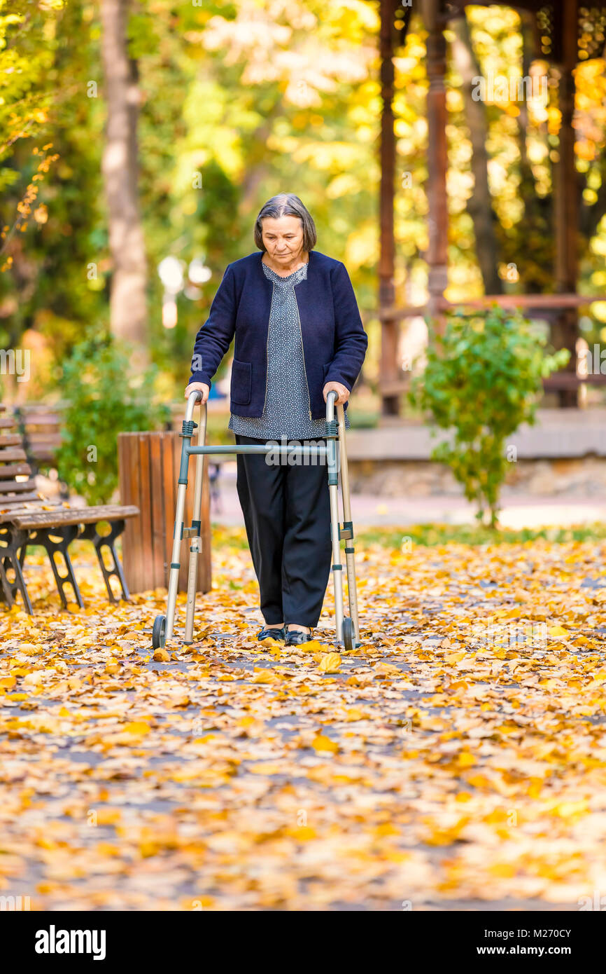 Senior woman with walker walking outdoors in autumn park. Stock Photo