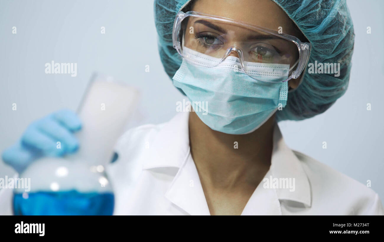 Female chemist holding flask with blue evaporating liquid in hand, experiment Stock Photo