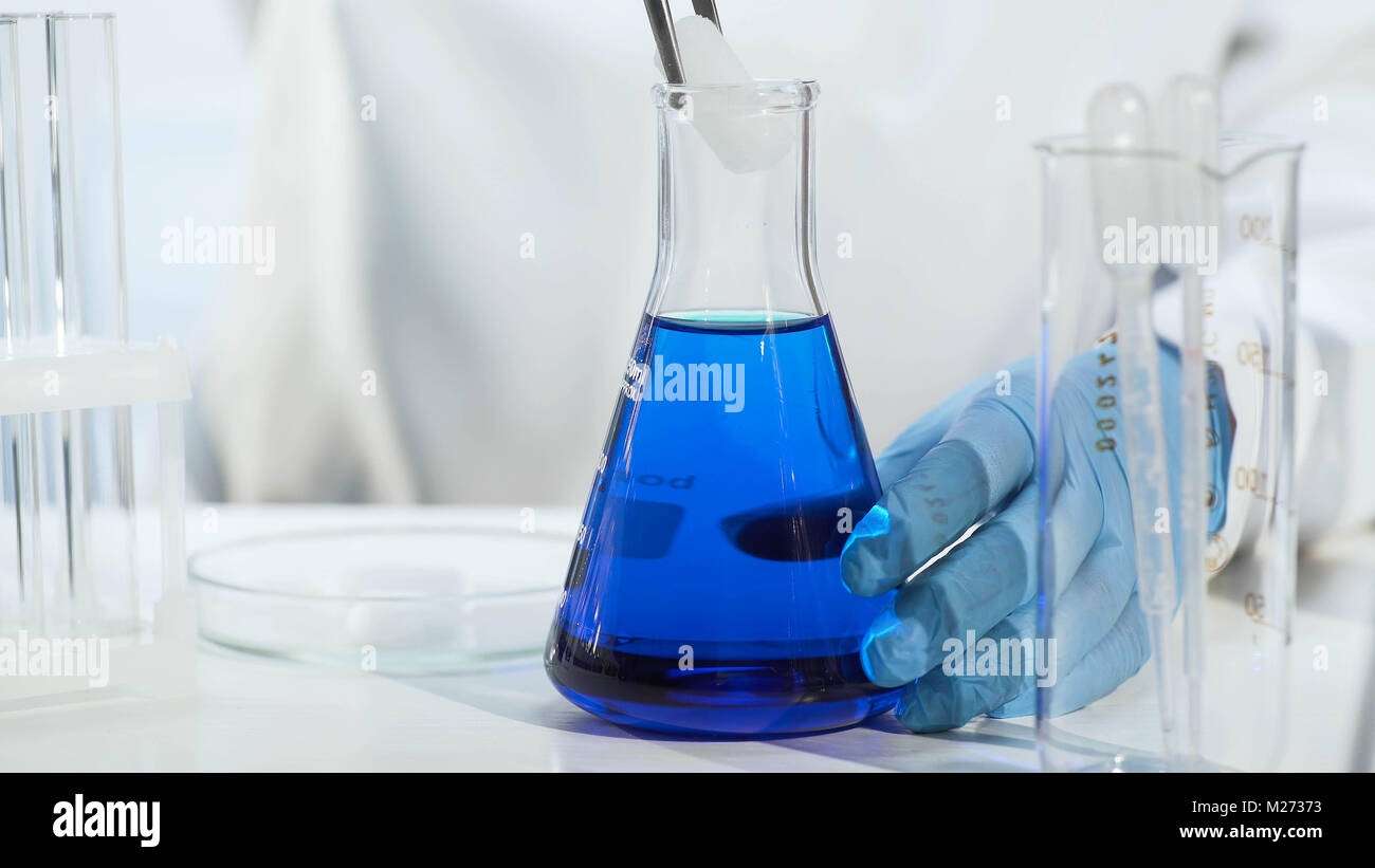 Chemistry teacher putting dry ice into blue liquid in conical flask, close-up Stock Photo