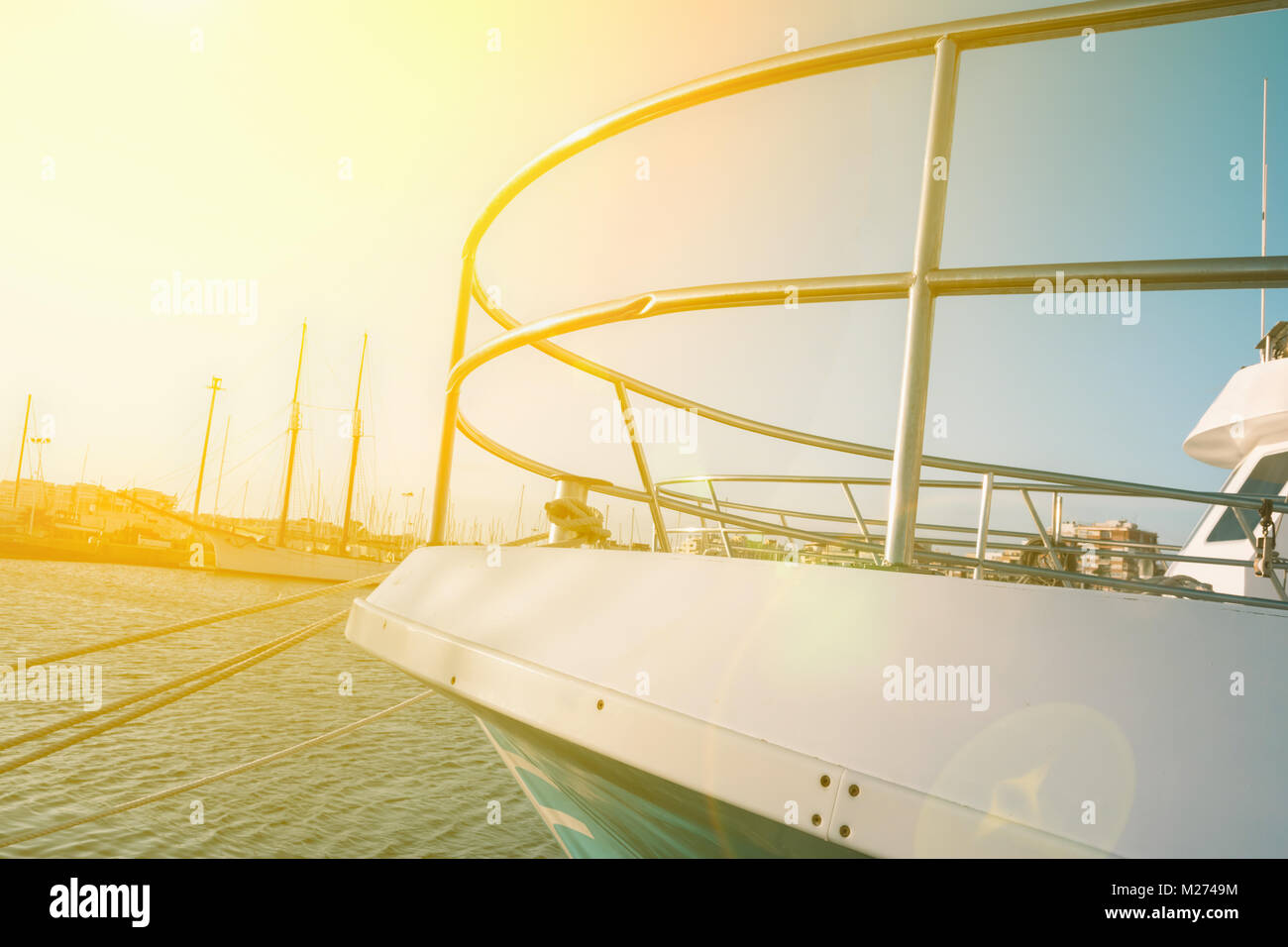 Large New Beautiful Yacht Moored in Dock at Mediterranean Sea. Latral Side View of Boat Bow Nose. Bright Golden Sunlight Flare Blue Sky Calm Sea Stock Photo