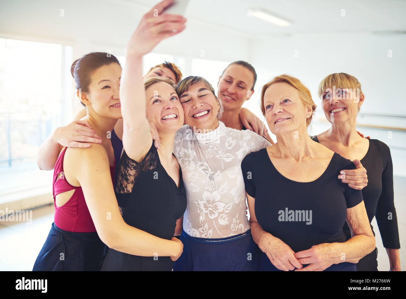 Mixed age group of smiling women standing arm in arm together in a dance studio taking a selfie Stock Photo