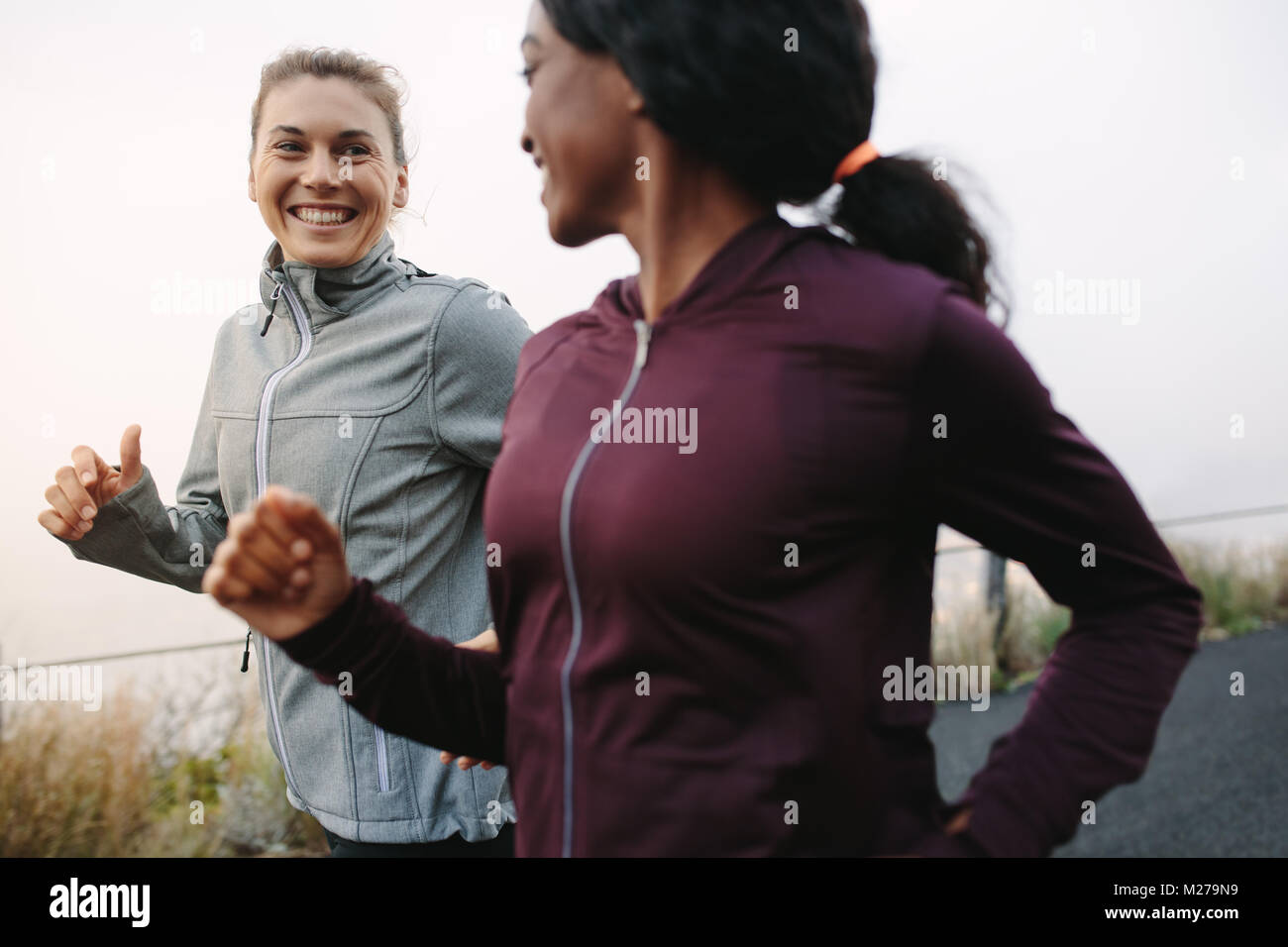 Two happy women going for sunrise running. Women in track suits running on road. Stock Photo