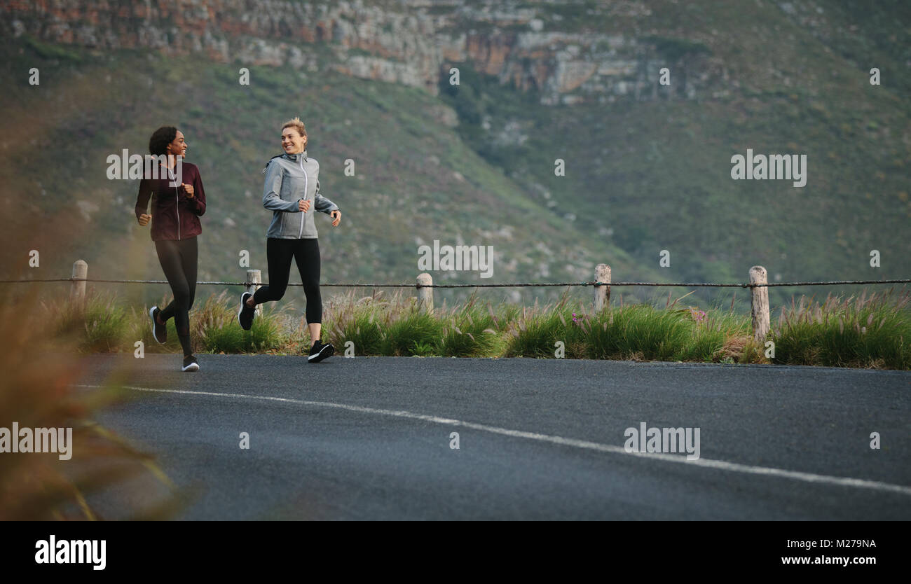 Two women going for an early morning run. Fitness runners in track suits running on road. Stock Photo