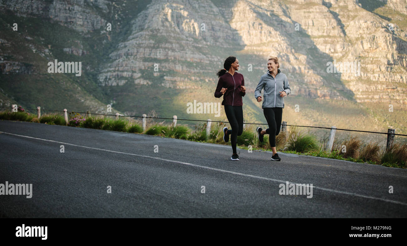 Women running on road early in the morning with hills in the background. fitness women jogging on road. Stock Photo