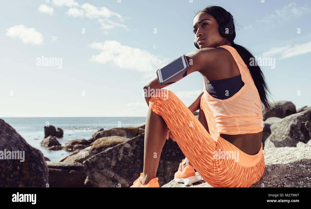 Fit young woman sitting over rocks after workout session in morning ...