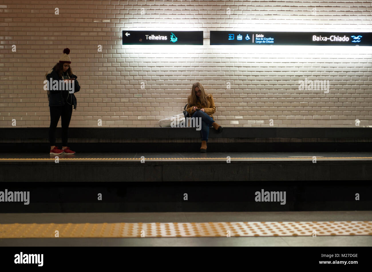 Young women using cell phones in metro station. Baixa Chiado, Lisbon, Portugal Stock Photo