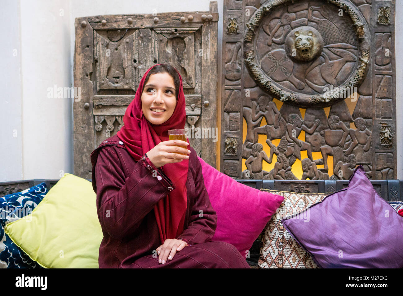 Arab woman in traditional red clothing with hijab on her head drinking a tea in traditional middle eastern ambient Stock Photo