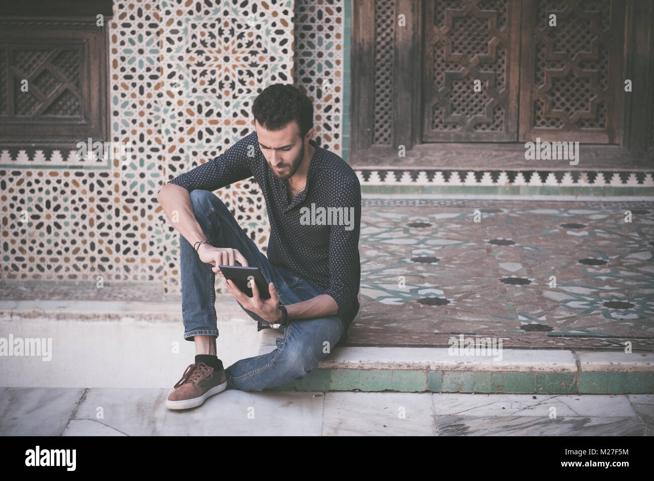 Young Muslim man in casual clothing working on tablet in traditional Arabian ambient Stock Photo