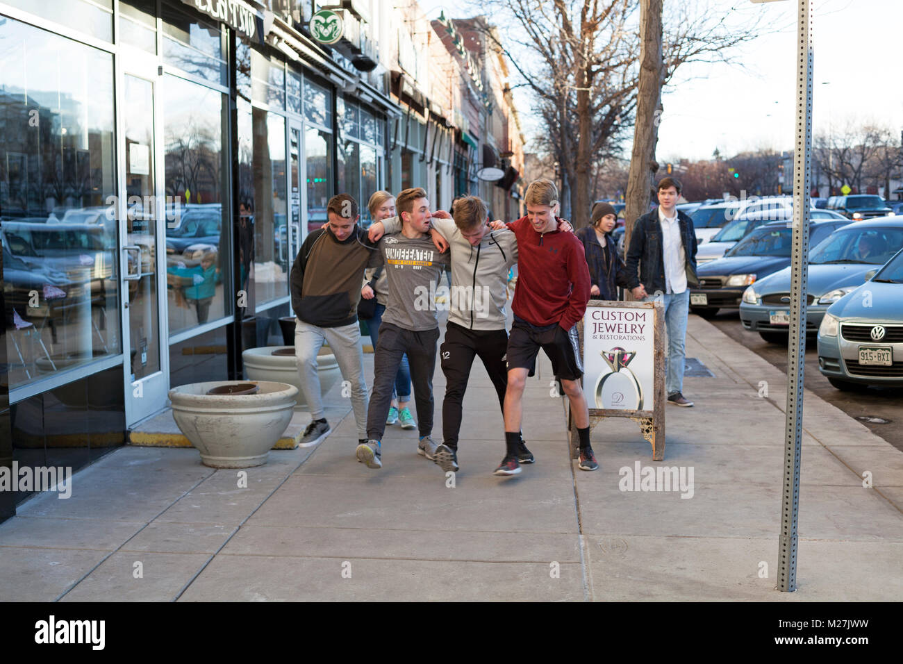 A group of friends locks arms and sidestep down the sidewalk in Fort