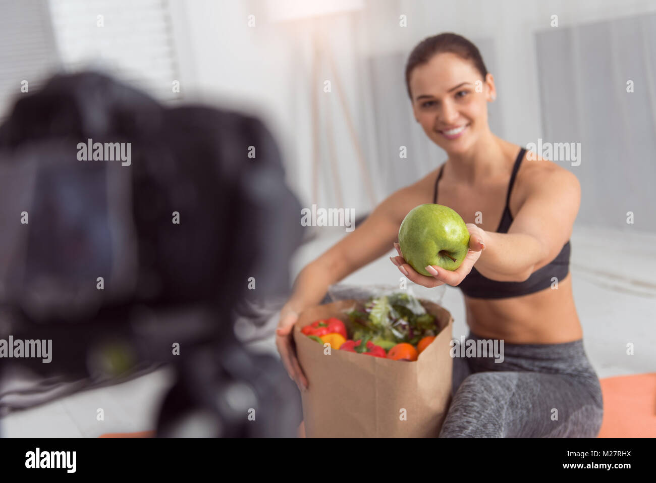 Cheerful blogger talking about an apple while making a video Stock Photo