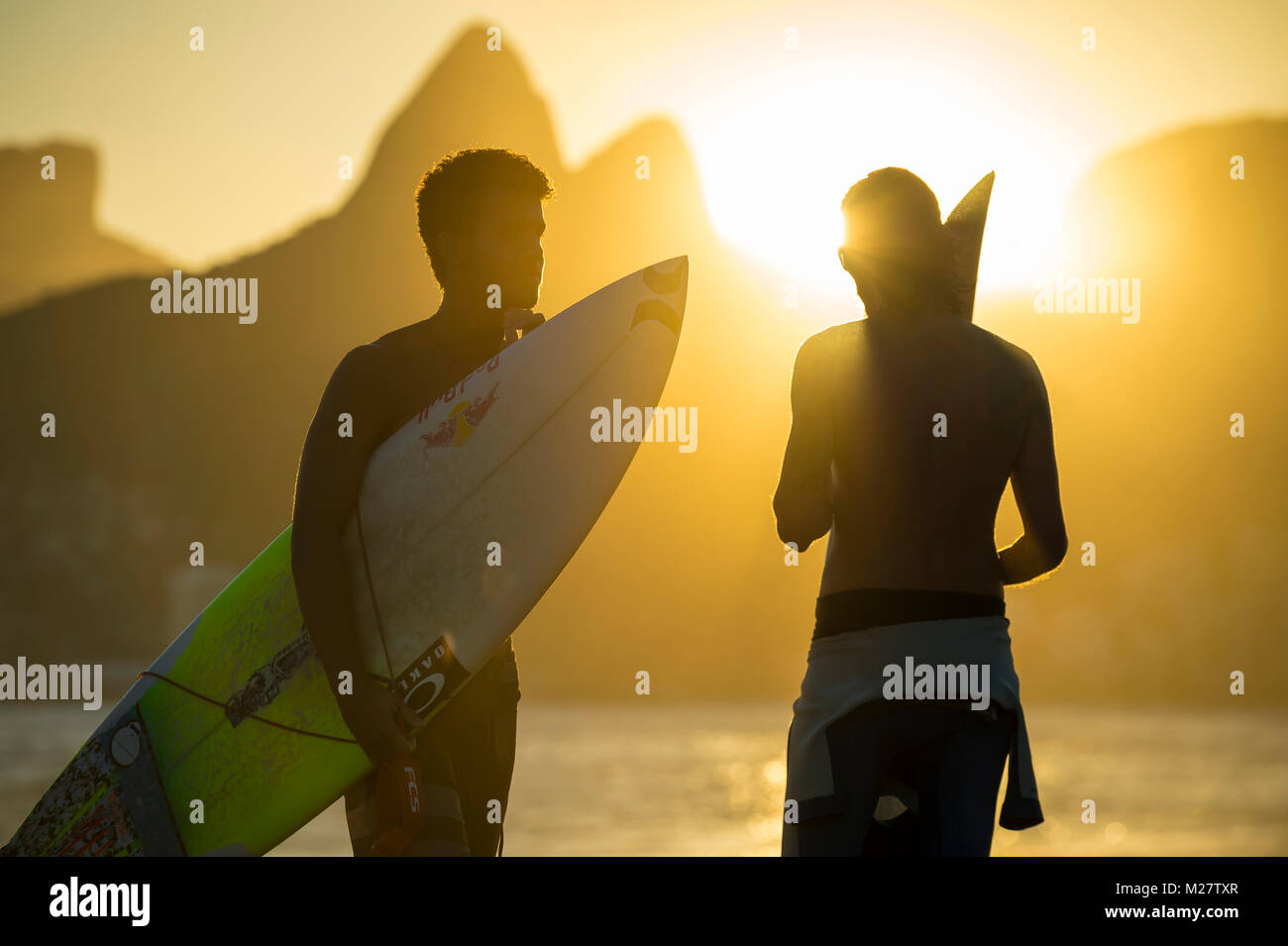RIO DE JANEIRO - MARCH 20, 2017: Sunset silhouettes of two young surfers with surfboards at Arpoador with two brothers mountains in the background Stock Photo