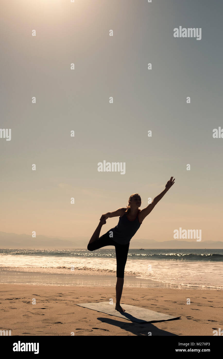 A young woman is exercising a stand up yoga pose at a beach Stock Photo