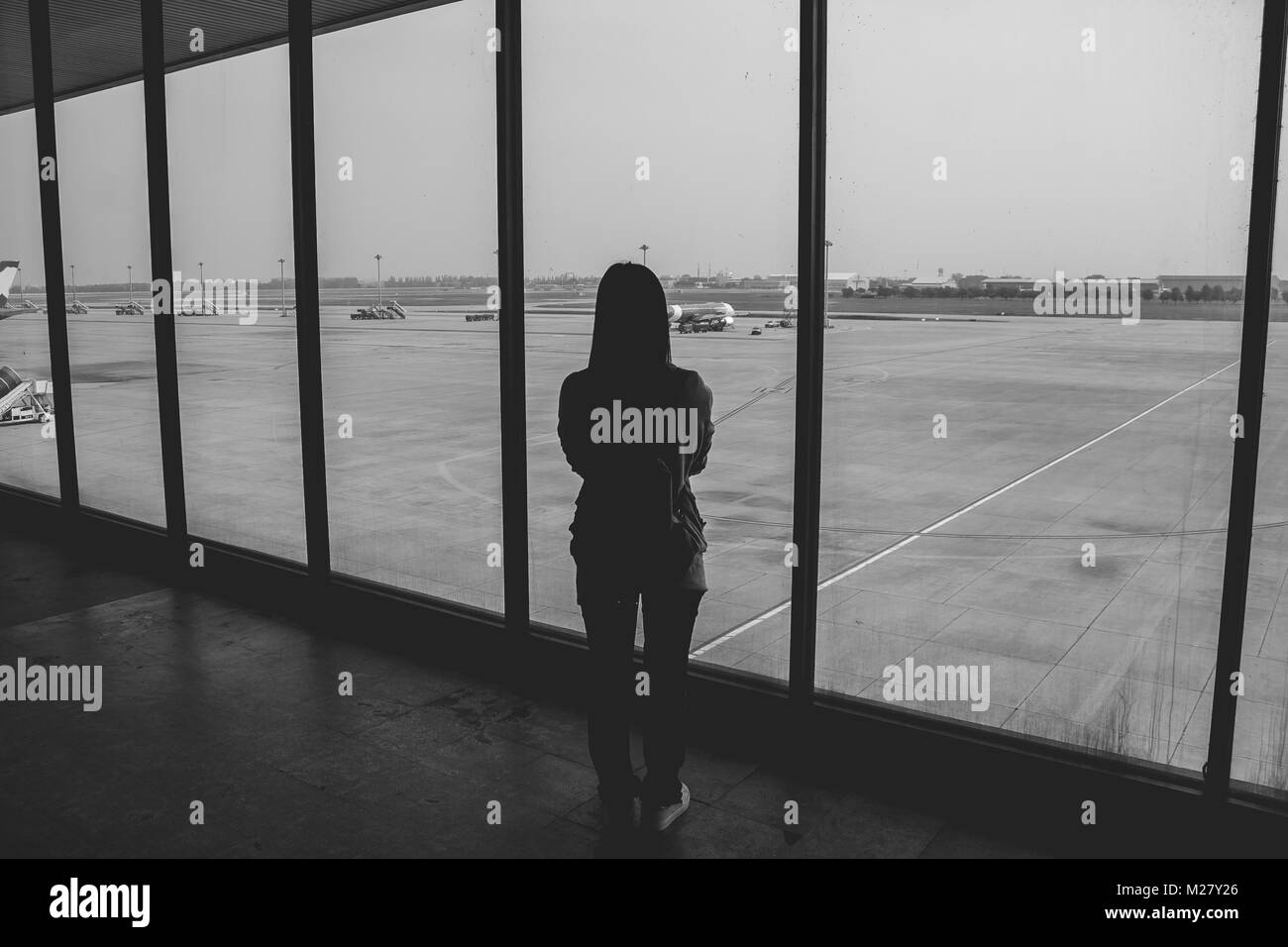 Woman standing in the airport terminal and looking at airplanes while waiting at boarding gate before departure. Stock Photo