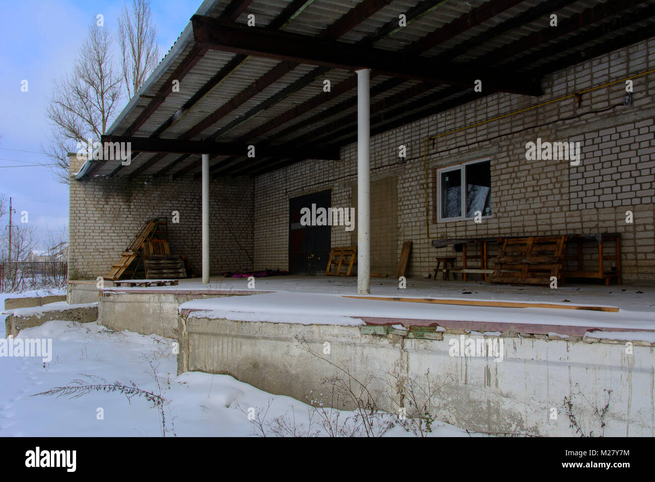 A platform for loading and unloading materials of the destroyed and abandoned bakery building against the background of winter trees and a blue cold w Stock Photo