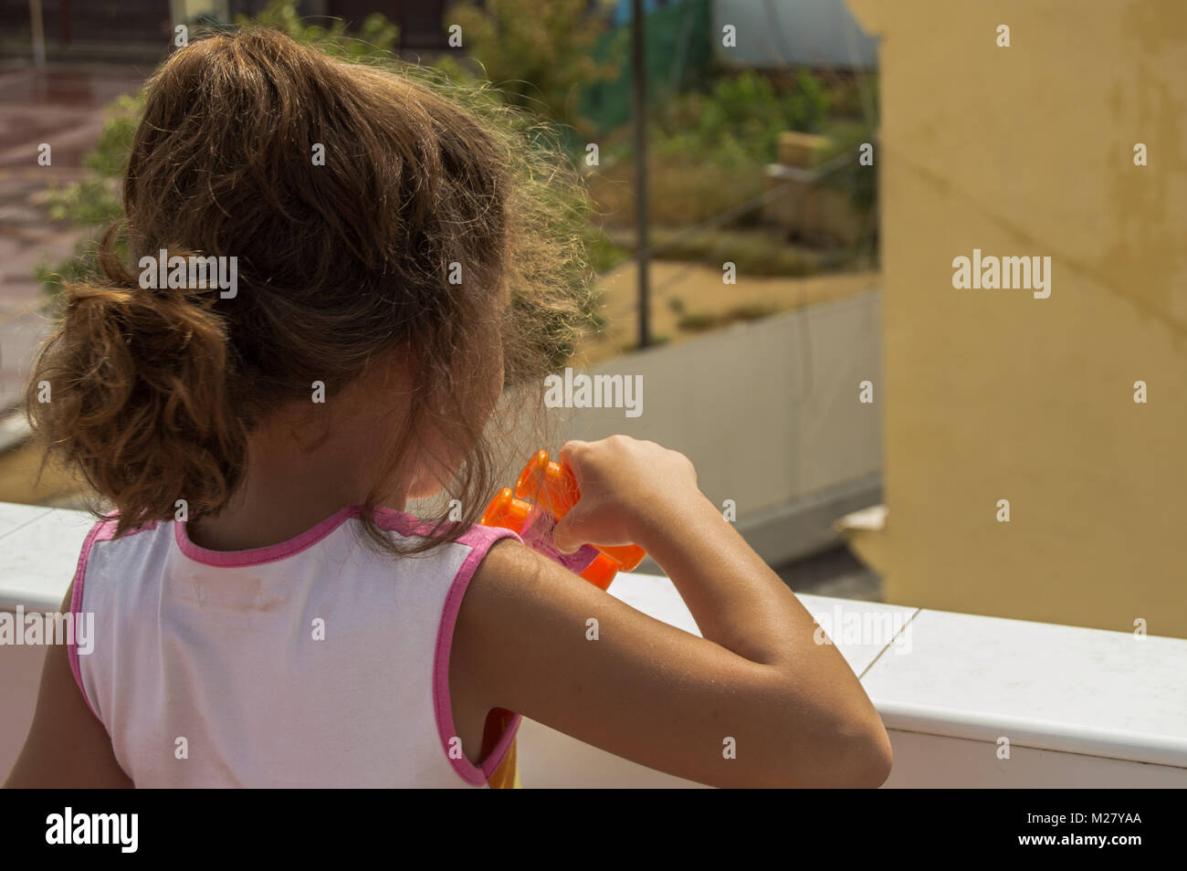 Little blond girl with curly hair playing with toy prismatic from the roof of a house on a sunny day. Stock Photo