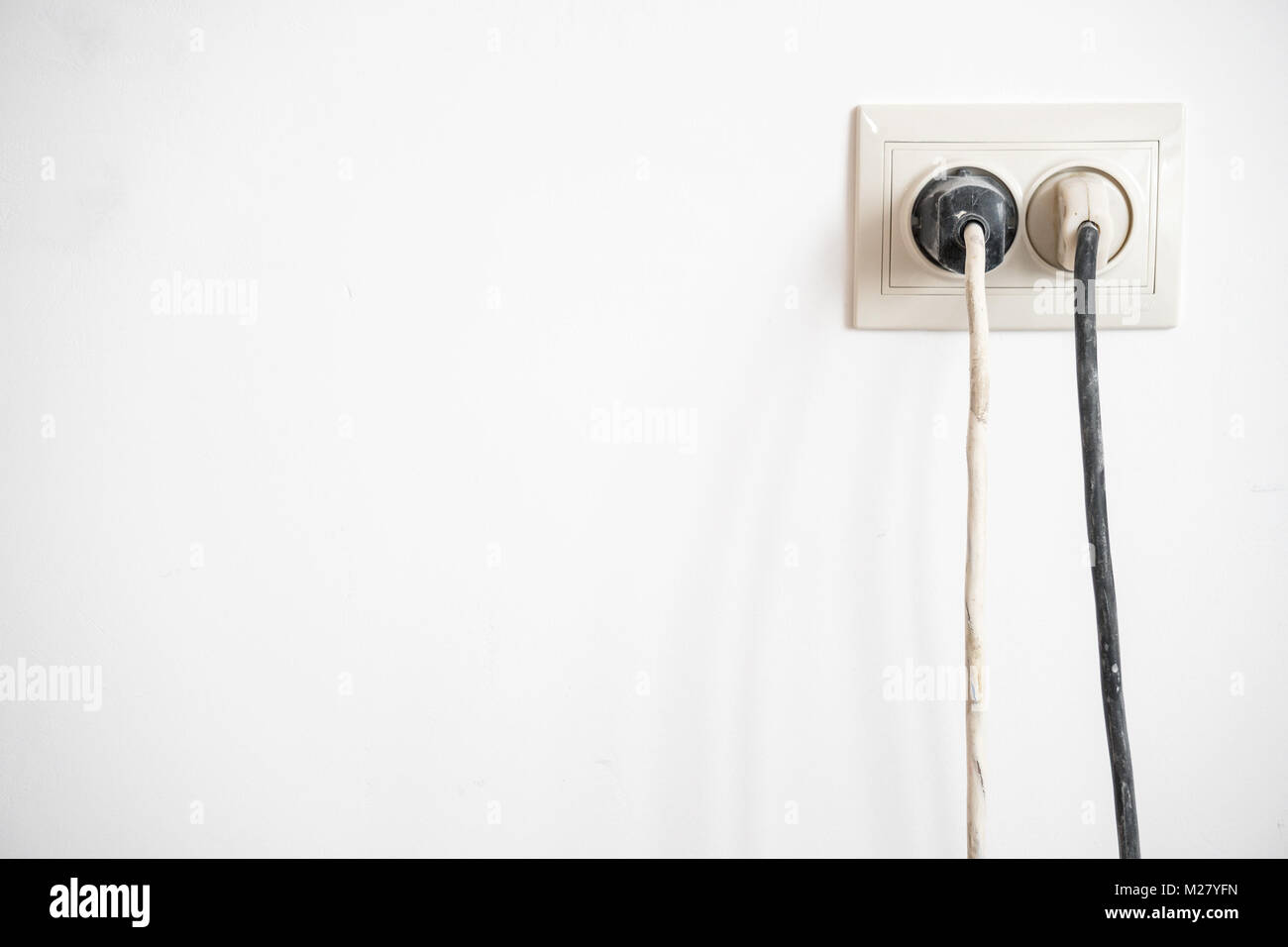 Electric socket with two stuck electric plugs on a white wall. Power