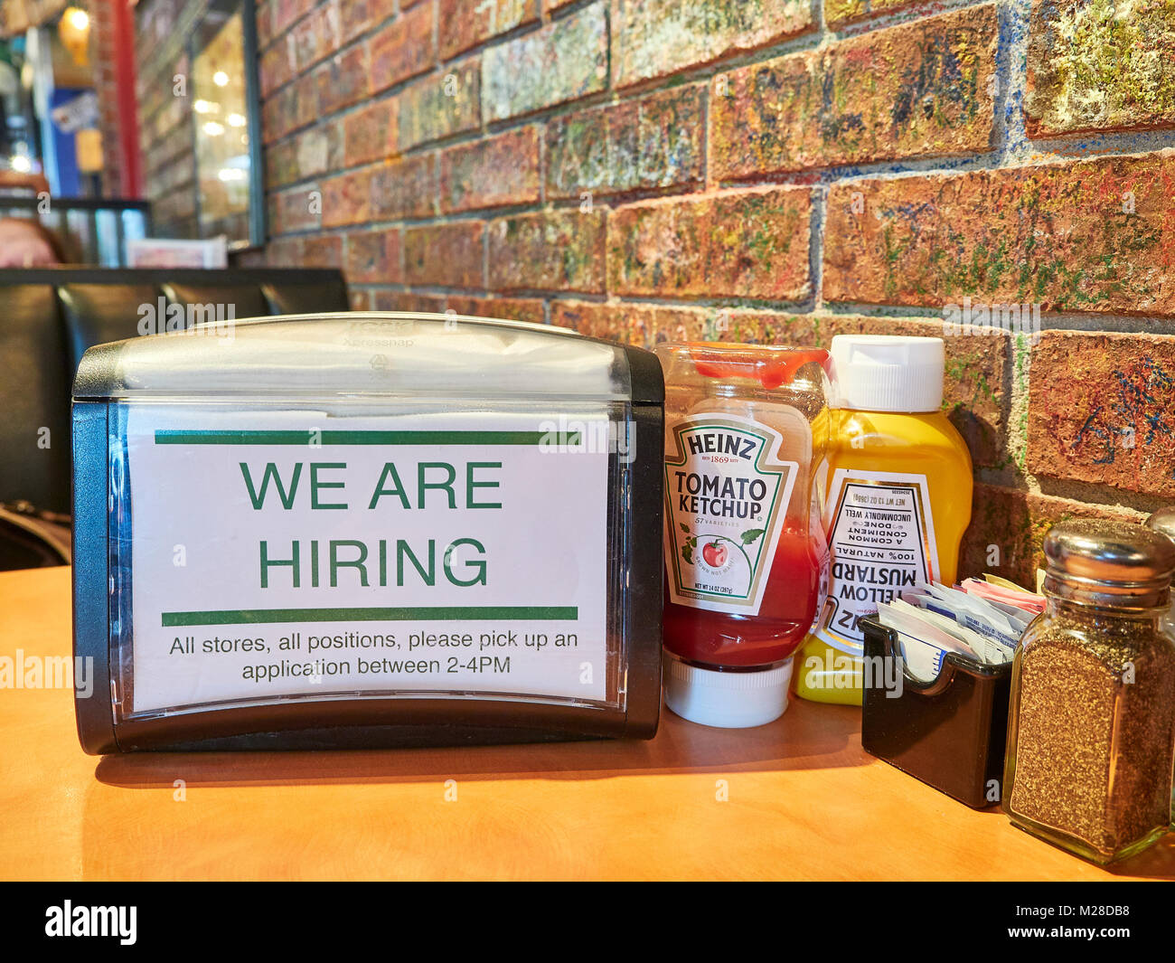 Inside or interior of restaurant table and napkin holder with we are hiring or a help wanted sign in Niffer's Restaurant, Auburn Alabama, USA. Stock Photo