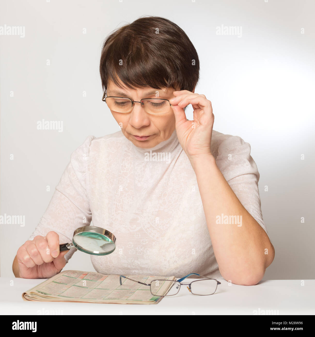 Vision problems. Woman with glasses and a magnifying glass reading a