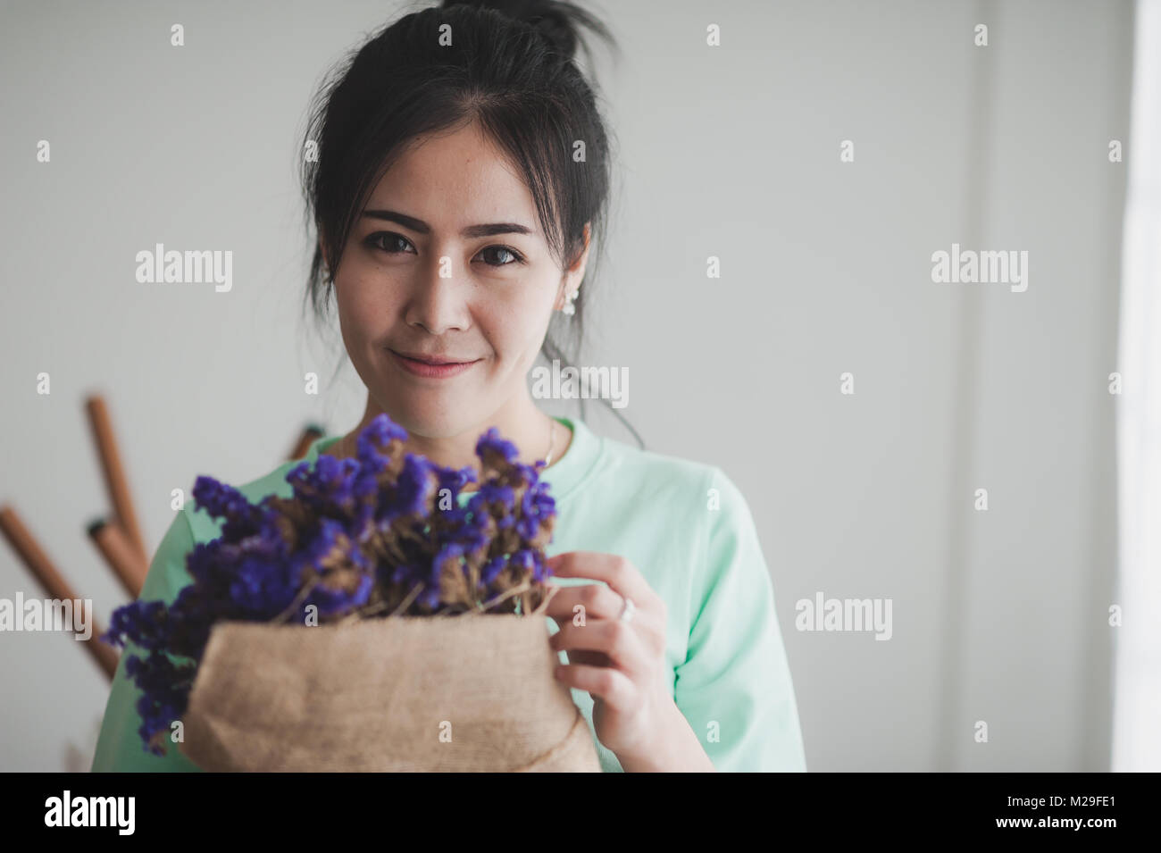 Young beautiful Asian woman in light green shirt hold flowers in her hands in morning time with photo filter effect. Person gesturing with positive em Stock Photo