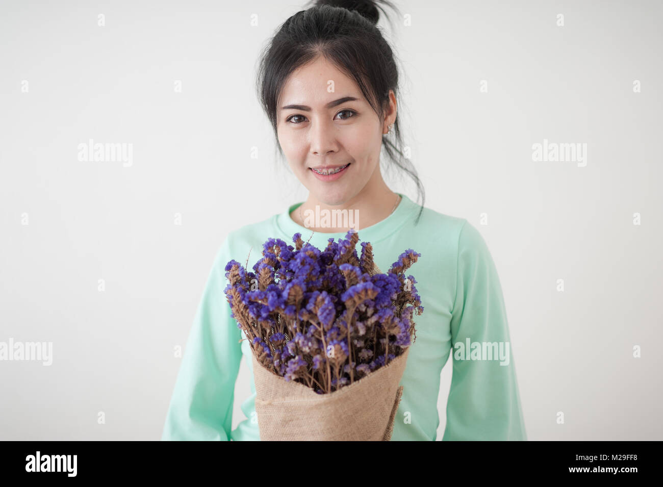 Young beautiful Asian woman in light green shirt hold flowers in her hands in morning time with natural lighting. Person gesturing with positive emoti Stock Photo