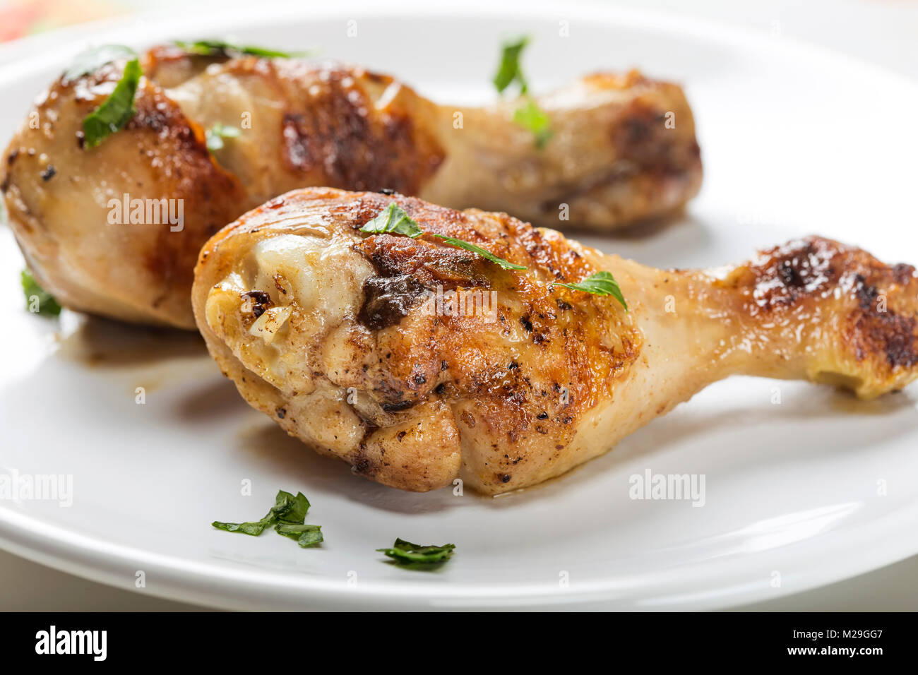 Closeup of two grilled chicken drumsticks with parsley on white palte Stock Photo
