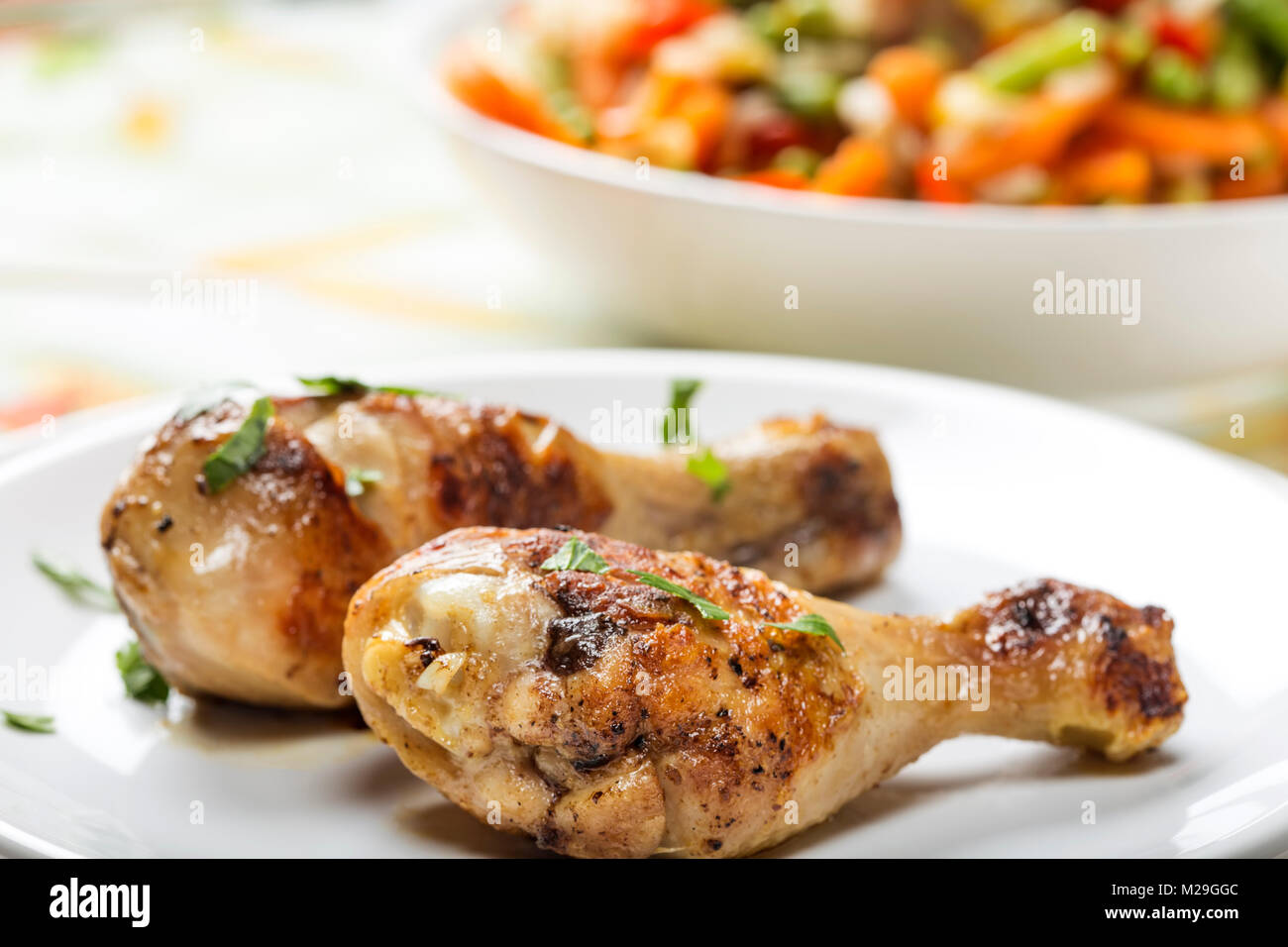 Closeup of two grilled chicken drumsticks with parsley on palte and bowl with salad in background Stock Photo