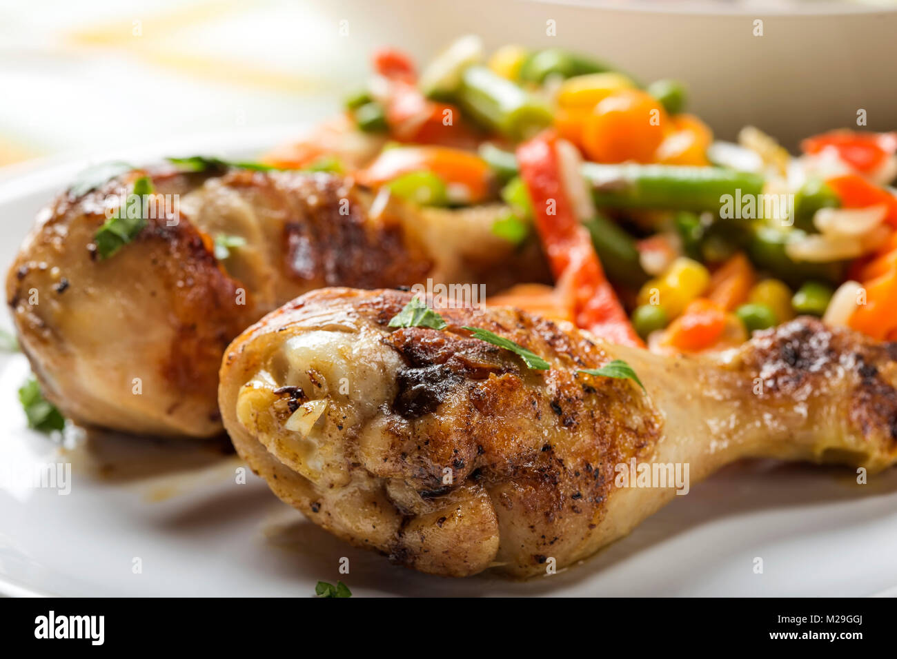 Two grilled chicken drumsticks on palte with vegetables Stock Photo