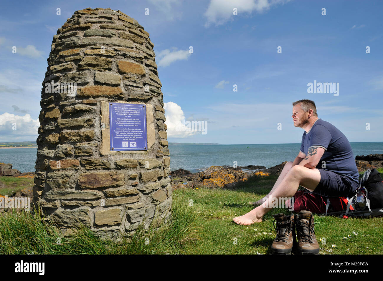 A walker rests his weary feet at the Great Outdoors Challenge 25th anniversary cairn at Scurdie Ness Light Montrose, Angus, Scotland. Stock Photo