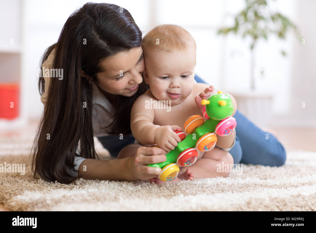 Mother and her baby son play with toy in cosy children room Stock Photo