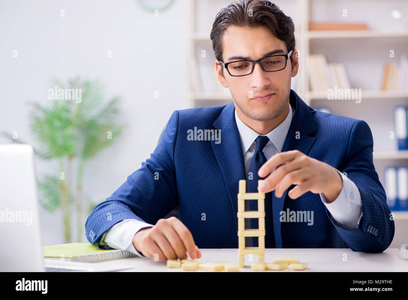 Young businessman building domino tower in office Stock Photo - Alamy