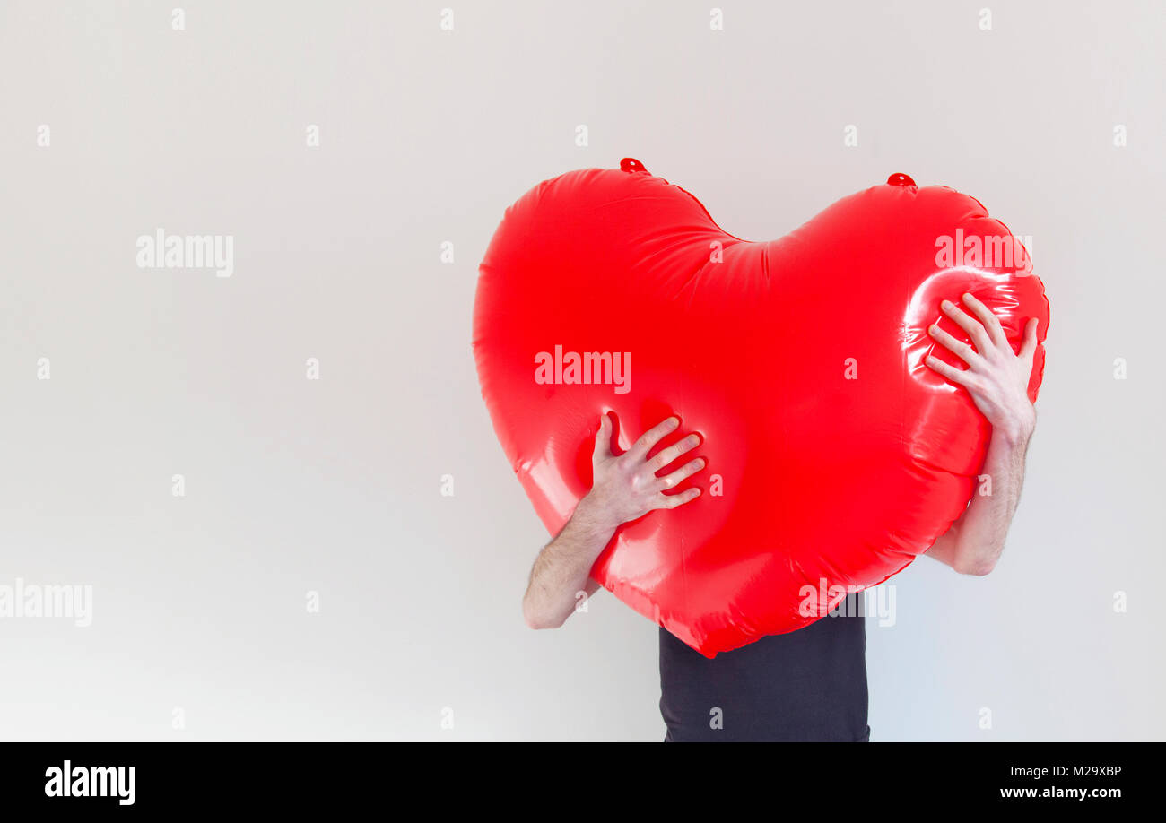 A person hugs a large red inflatable love heart. Health and love concept Stock Photo