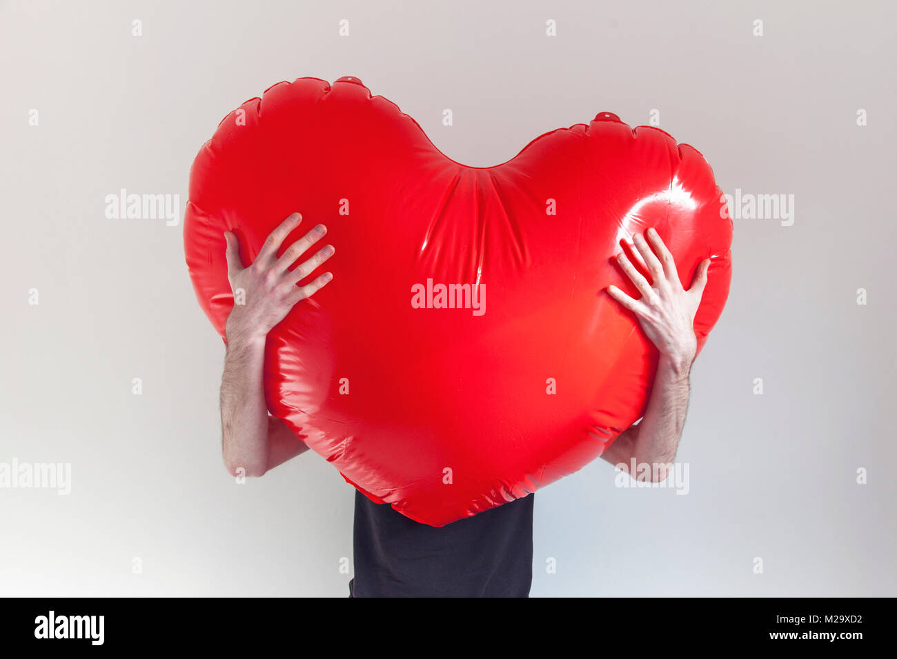 A person hugs a large red inflatable love heart. Health and love concept Stock Photo
