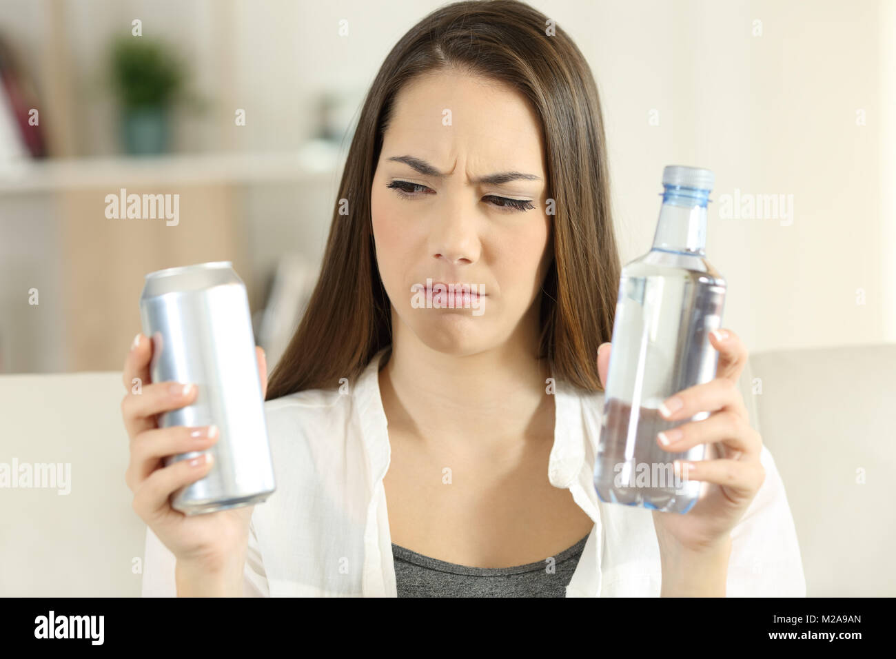 Front view portrait of a confused girl deciding between soda refreshment and water bottle at home Stock Photo