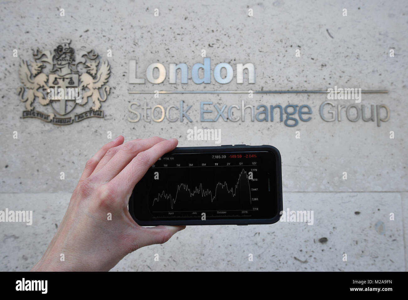 A view of the Stocks app on an iPhone against the London Stock Exchange sign in the City of London, as the FTSE 100 Index crashed on opening by more than 230 points to 7,104.94 as inflation fears continue to rock global markets. Stock Photo
