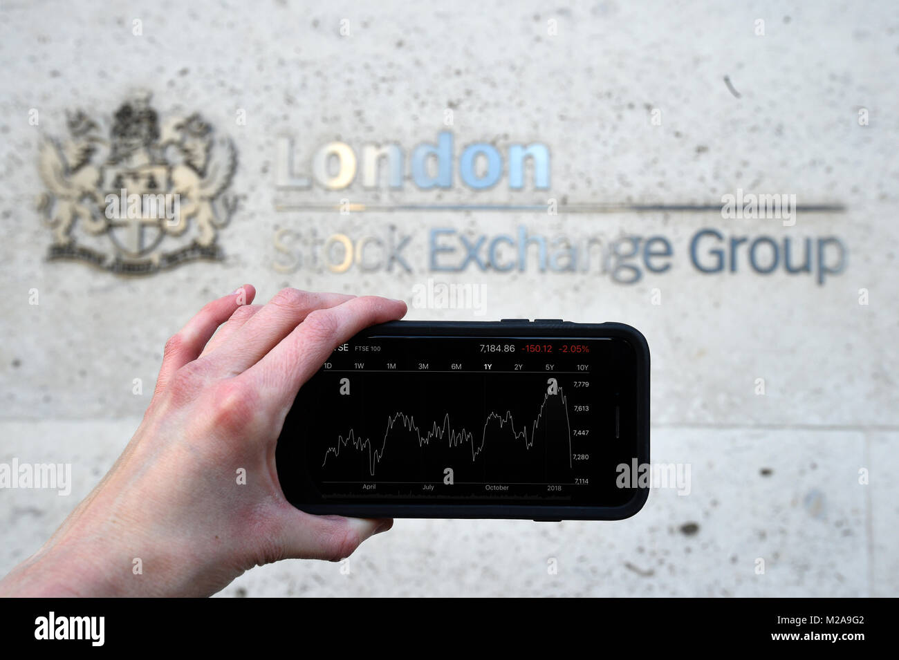 A view of the Stocks app on an iPhone against the London Stock Exchange sign in the City of London, as the FTSE 100 Index crashed on opening by more than 230 points to 7,104.94 as inflation fears continue to rock global markets. Stock Photo