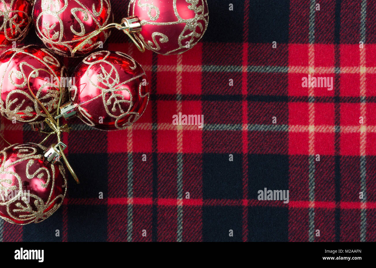 Top view of several Christmas ornaments atop a red, black and white tartan cloth with room for a message. Stock Photo