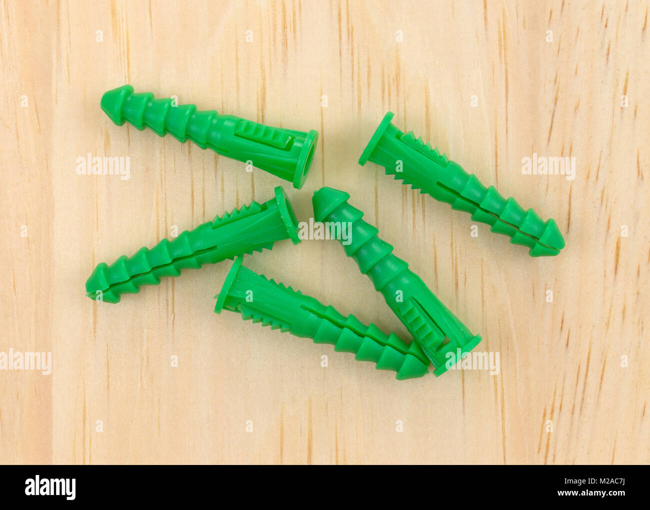 Top view of a group of green plastic drywall anchors on a pine board. Stock Photo