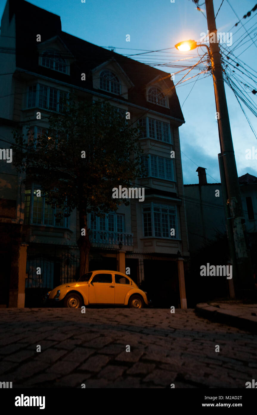 A yellow Volkswagen Beetle illuminated by a streetlight at dusk in La Paz, Bolivia Stock Photo