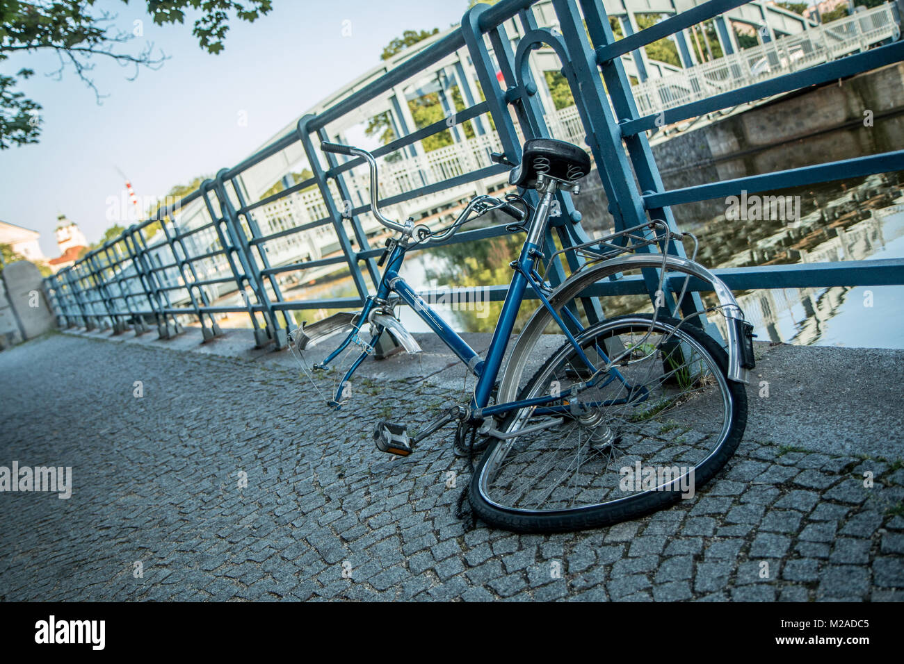 A broken bike is locked to the railing at the river in the city center