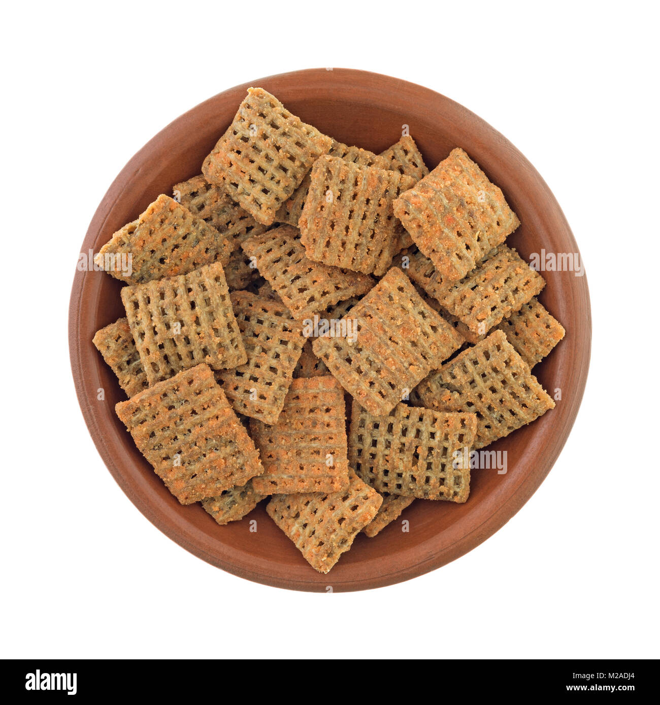 Top view of a small bowl filled with cheddar cheese flavored square wheat crisps isolated on a white background. Stock Photo