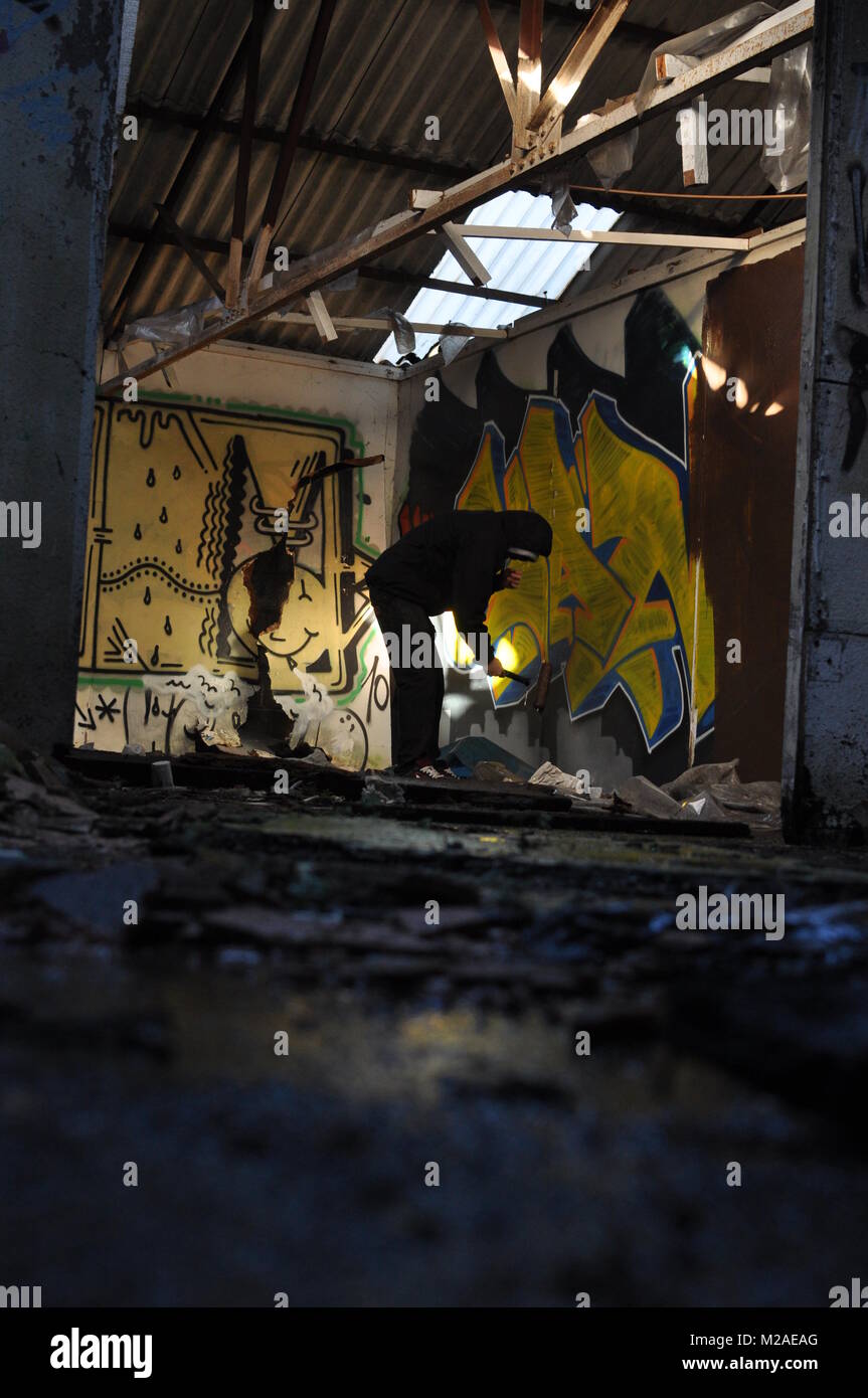 A graffiti artist painting a piece with a paint roller in an abandoned