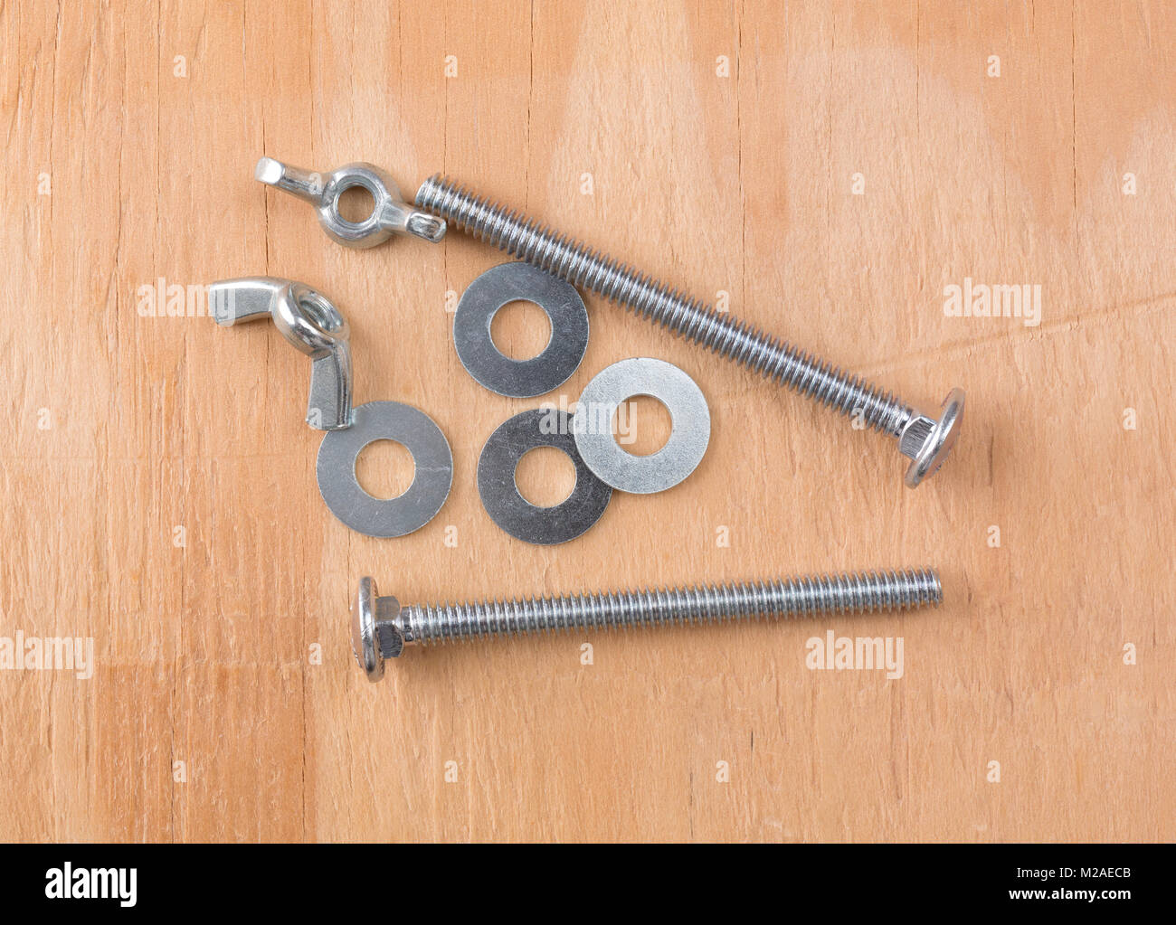 Top view of a group of wing nuts, long bolts and washers atop a plywood