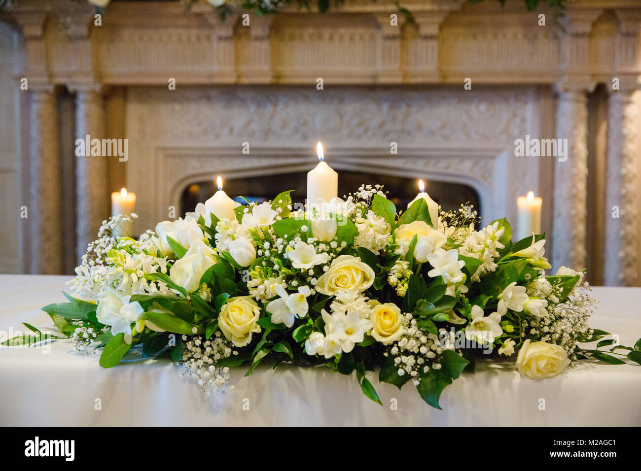 Cream floral arrangement with lit candles on wedding reception table Stock Photo