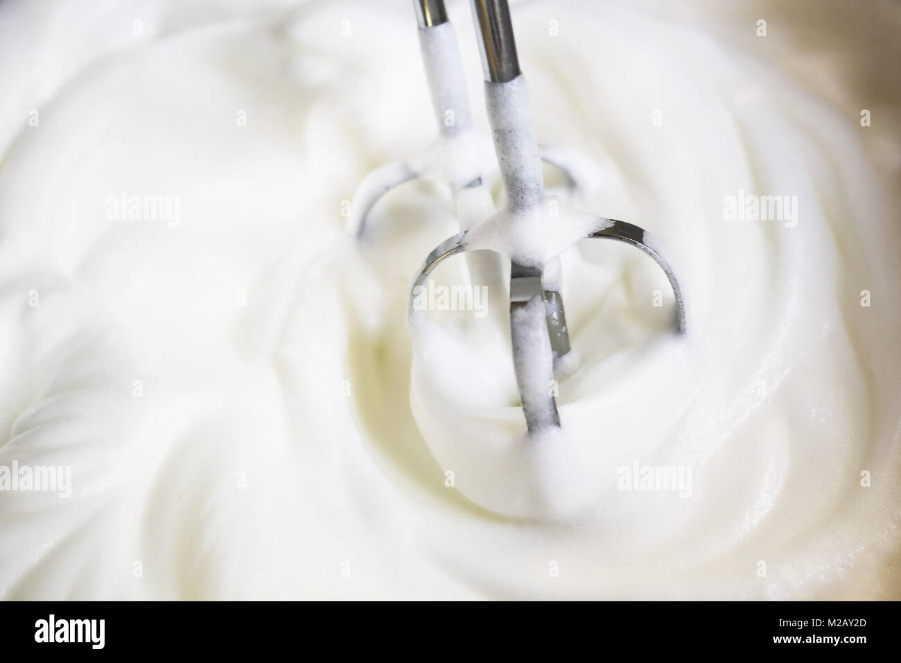 Mixer beaters partly emersed in whipped egg whites that have just been beaten until they are stiff Stock Photo