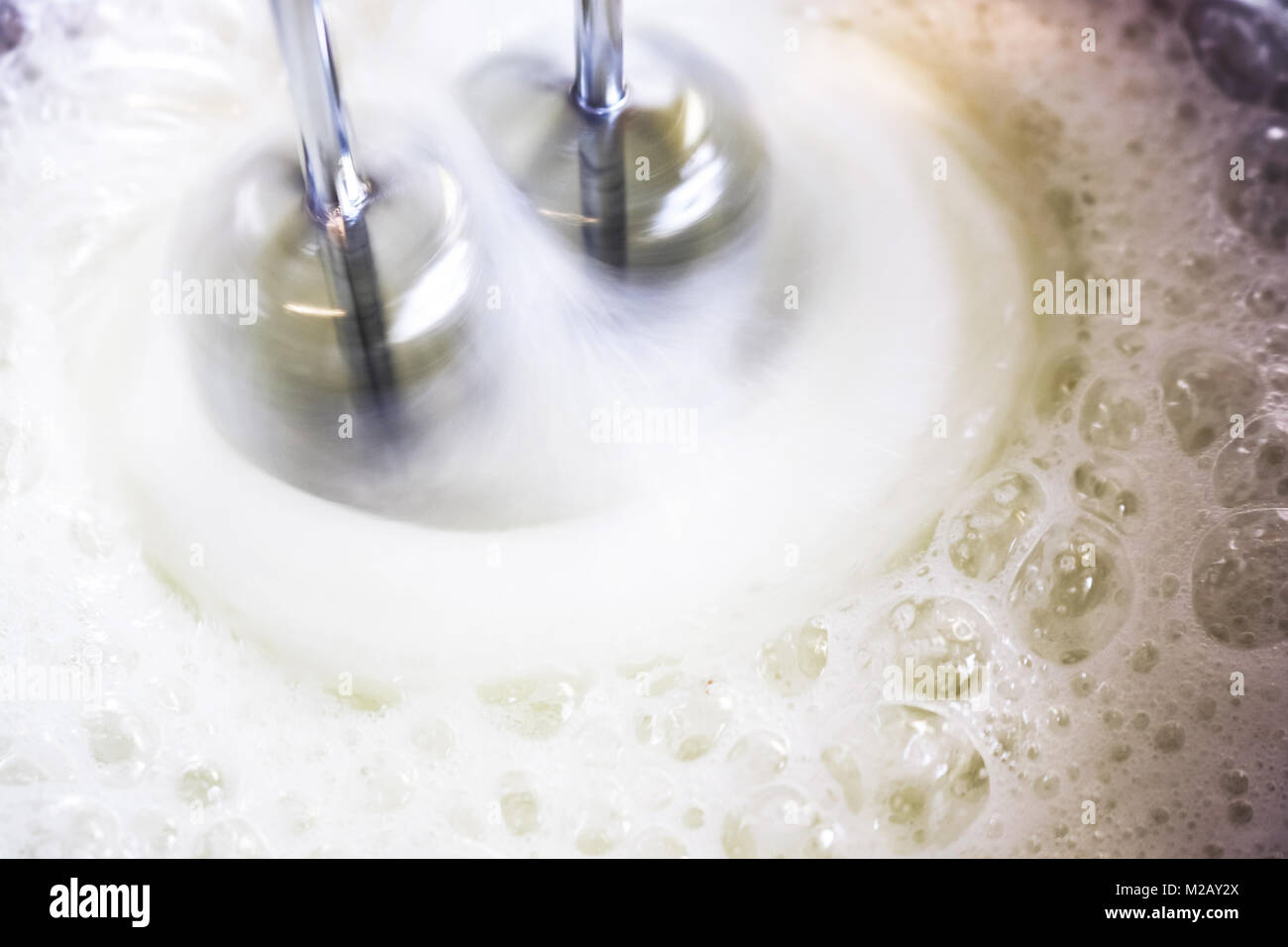 Mixer in motion whipping frothy egg whites in a bowl to make meringue Stock Photo